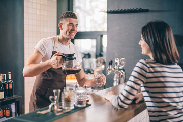 Friendly barista holding glass coffee jug and smiling
