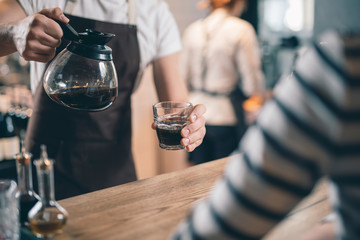 Close up of coffee jug and glass in hands of barista