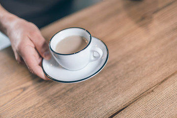 Hand putting cup of hot chocolate on the wooden surface