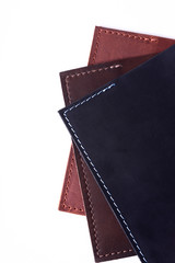 A parts of three handmade leather passport covers isolated on white background. Closeup view. Covers are dark blue, red and brown.