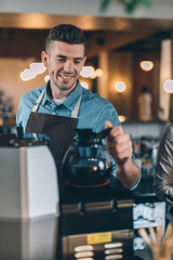 Close up of smiling barista putting coffee jug on the coffee machine