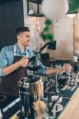 Friendly barista smiling while holding empty glass and coffee jug