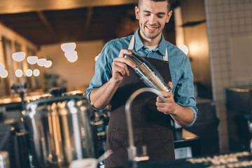 Young smiling bartender using cocktail shaker at work