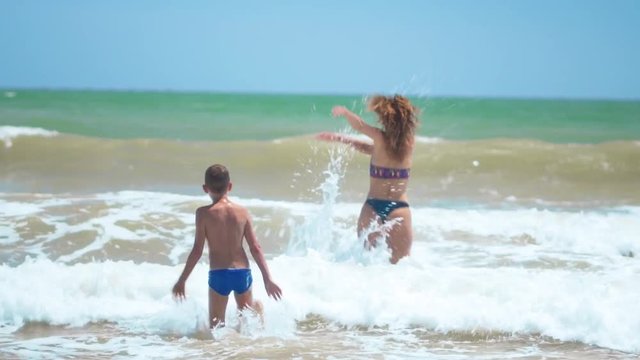 Happy family mom and baby running barefoot on wet sand, rear view. Mom and baby holding hands together runing on beach.