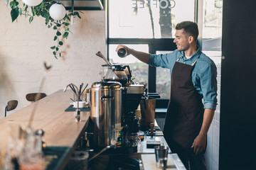 Young barista sifting coffee into the grain tank and smiling