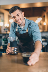 Friendly young barista smiling to the camera and giving pour over - obrazy, fototapety, plakaty