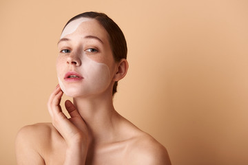 Beautiful girl with white mask on her face standing against beige background