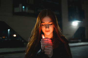 Young redhead woman with a burning lighter in the night city.