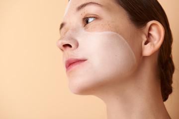 Lovely girl with white mask on face standing against beige background