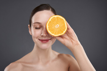 Charming young woman with freckles covering eye with orange