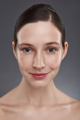 Beautiful smiling girl with freckles standing against gray background