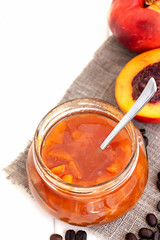 Homemade nectarine or peach jam confiture in glass jar and spoon on white wooden background. Selective focus. Copy space.