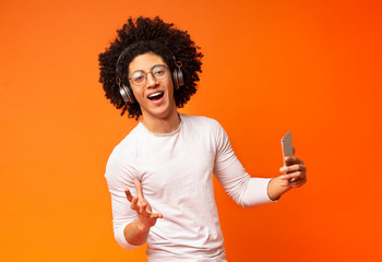 Bushy millennial guy singing with phone on orange background