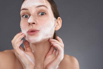Cute girl with freckles washing her face with soapsuds