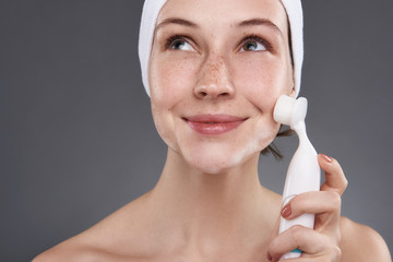 Smiling girl with freckles using pore cleansing brush after bath