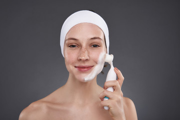 Cute girl in white headband using pore cleansing brush after bath