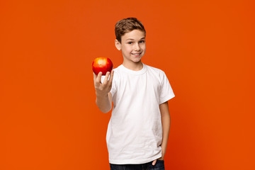 Positive little boy offering fresh red apple on camera