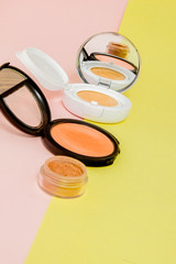 Make up products spilling on to a bright yellow and pink background with copy space