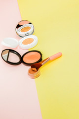 Make up products spilling on to a bright yellow and pink background with copy space