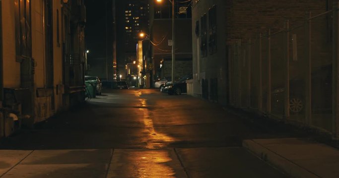 Establishing shot of a dark alleyway at night. Atmospheric 4K footage. Shot on a cinema camera in RAW. No discernible faces or logos.