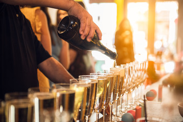 Waiter pouring champagne into glasses on party event in the bar