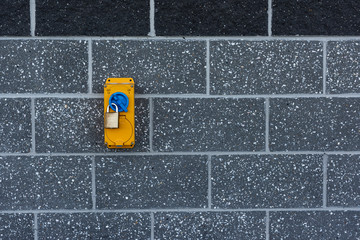 Padlocked yellow and blue power switch on a brick wall.