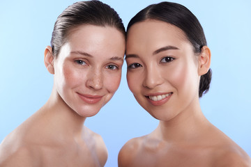 Waist up of charming interracial women situating against blue background