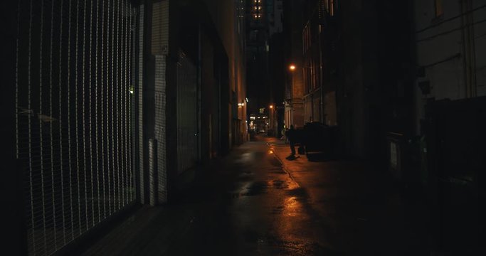 Establishing shot of a dark alleyway at night. Atmospheric 4K footage. Shot on a cinema camera in RAW. No discernible faces or logos.
