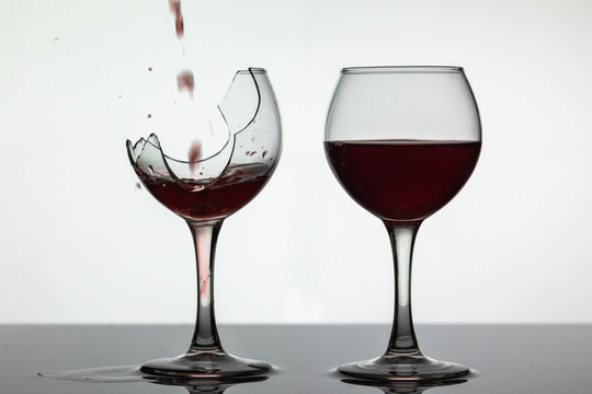 Red wine pouring into broken wine glass on the wet surface. Rose wine pour