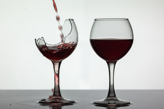 Red wine pouring into broken wine glass on the wet surface. Rose wine pour