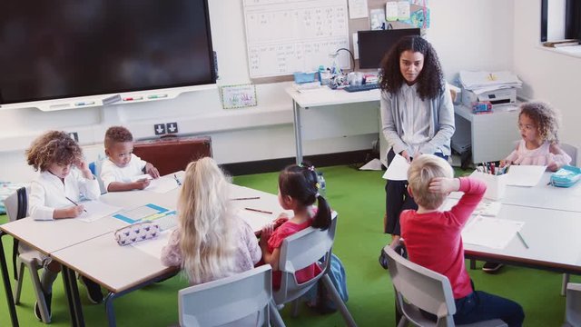 Smiling female infant school teacher sitting in front of class talking to school kids, elevated view