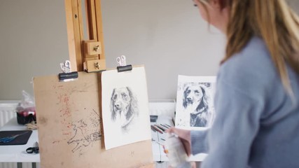 Female Teenage Artist Spraying Lacquer Fixative Onto Drawing Picture Of Dog In Charcoal