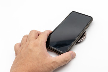 Hnad holding black mobile phone to charge on the black grossy round shape wireless charger isolated...