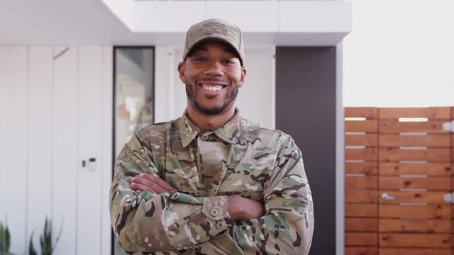 Millennial black male soldier steps towards camera, crosses arms and smiles to camera, close up