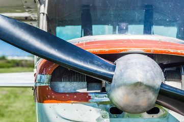 Small light utility aircraft, worn red and white paint, front view with propeller on sunny day.