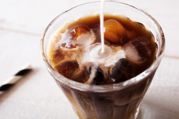 putting milk in iced coffee, close up