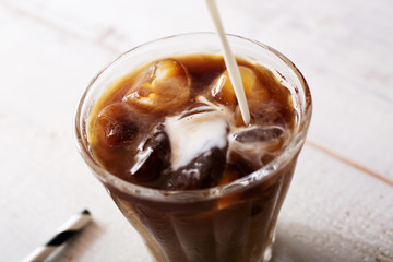 putting milk in iced coffee, close up