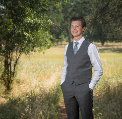 Smiling young man in business suit standing outside hands in pockets