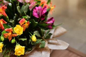 Close-up of a vibrant mixed flower bouquet with yellow roses and orange alstroemeria wrapped in rustic burlap fabric, bouquet with colorful roses, horizontal, flowers in a vase,  spring week