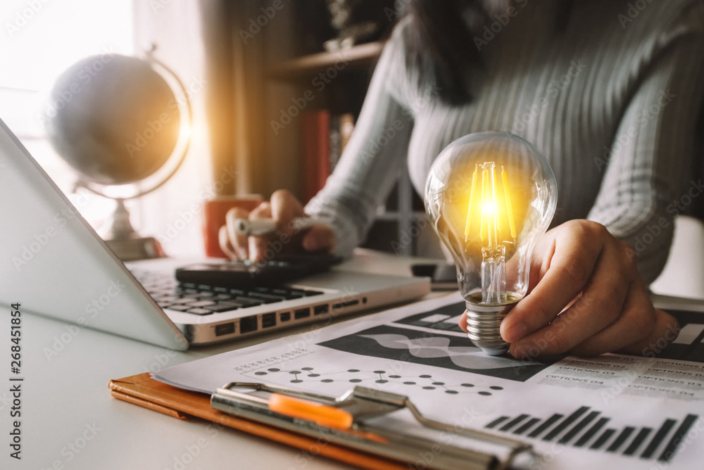 Poster business hand holding lightbulb with using laptop computer and money stack in office. idea saving en