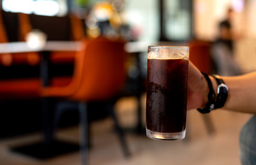 closeup hand holding cup of ice coffee in cafe with soft-focus and over light in the background