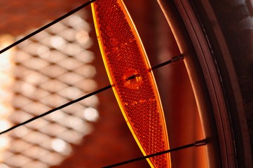 Fototapeta na wymiar orange traffic safety reflector in a bicyle wheel clamped in spoke in bright light