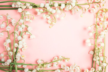 Frame of lily of the valley flowers on a pink background.