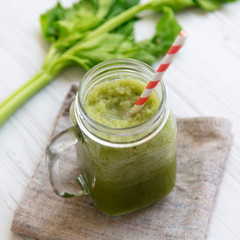 Glass jar of green celery smoothie on a white wooden surface, low angle view. Close-up.