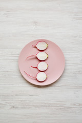 Radish slices on a pink plate over white wooden background, top view. Overhead, from above, flat lay.