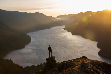 Person on mountain top overlooking lake at sunset with golden light