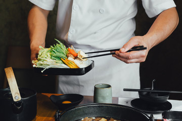 Chef pinching vegetables into hot pot by chopsticks before pouring soy soup.