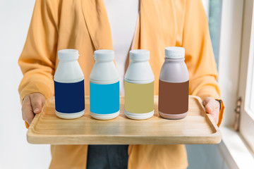 Woman holding bottles of pasteurized milk in blue, turquoise, gold and brown label color in wooden tray.
