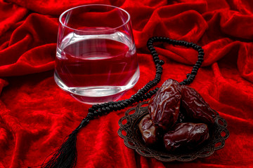 Muslim religious tradition, Ramadan month, Islam and break of the fast after sunset or Iftar concept theme with close up on a bowl of dried dates, prayer beads and a glass of water