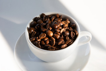 Coffee beans in coffee cup on white.
